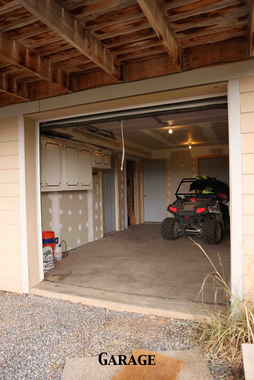 Unfinished garage space featuring a concrete floor, exposed ceiling joists, and built-in white cabinetry