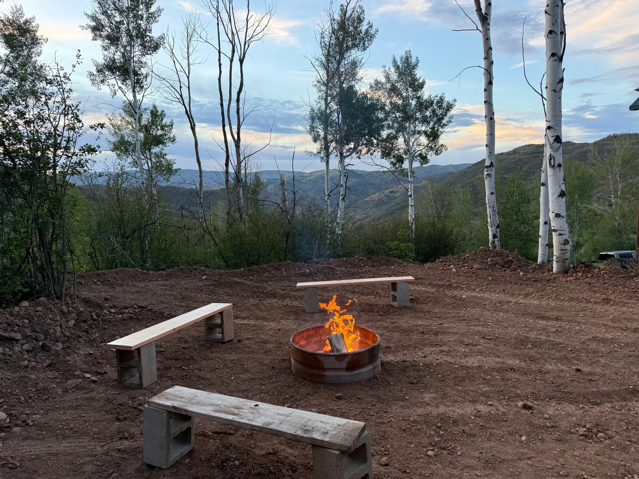 Outdoor fire pit area with three wooden benches on a natural ground surface