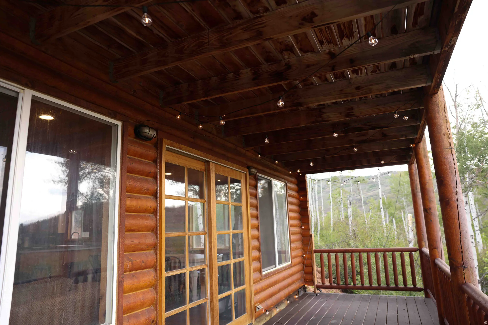 Expansive wooden deck featuring log column supports, a wooden railing, and string lighting