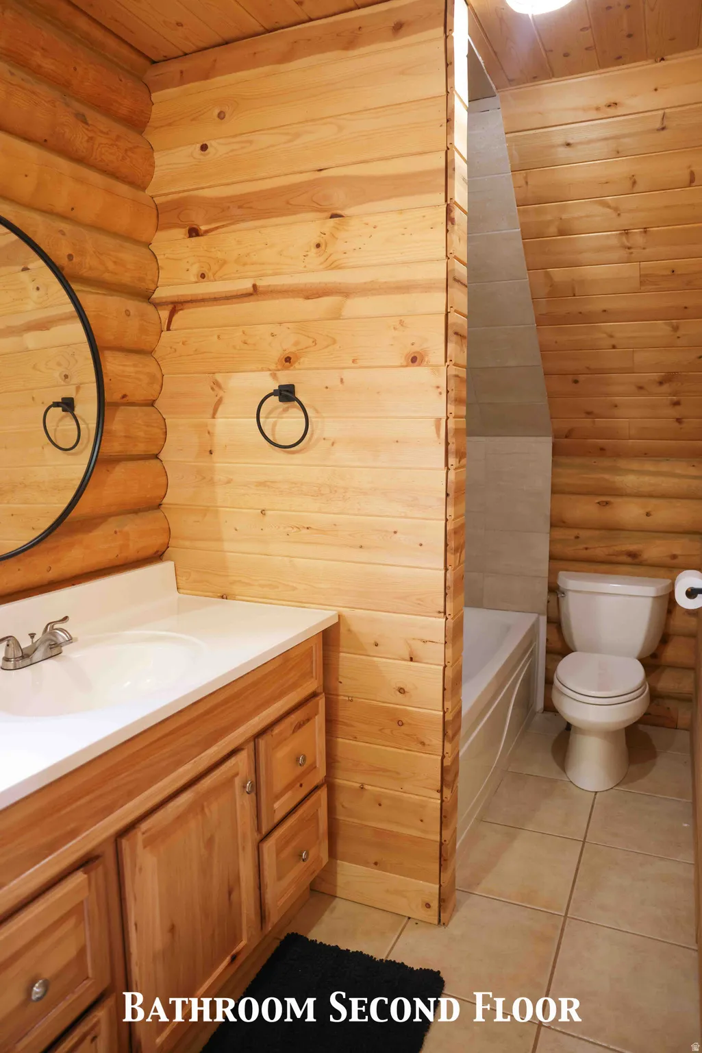 Bathroom featuring wood-finish walls, a vanity with a solid surface countertop and integrated sink, and tile flooring
