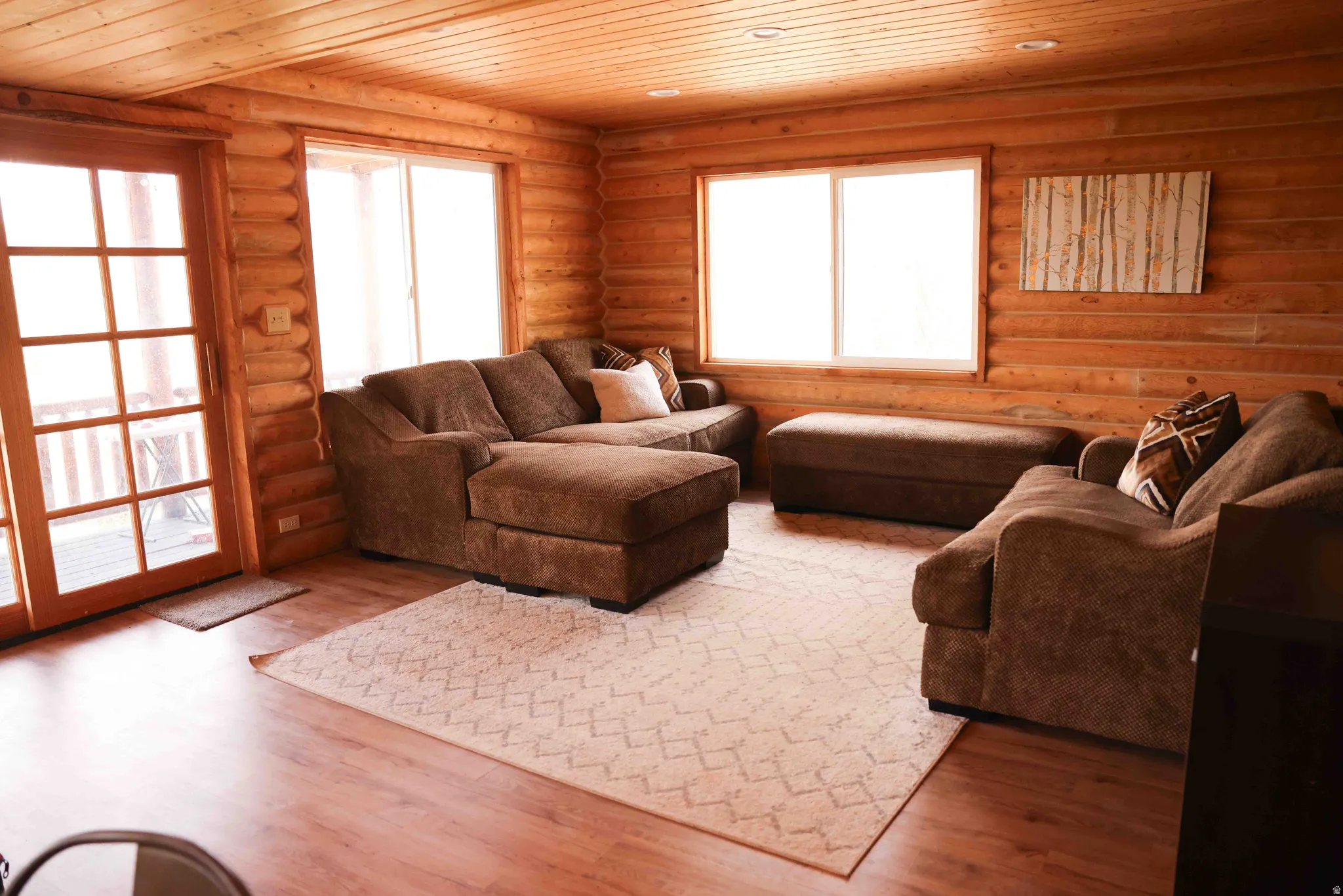 Living area featuring log walls, wood-finish flooring, a wood-paneled ceiling, and a glass sliding door opening to an outdoor area