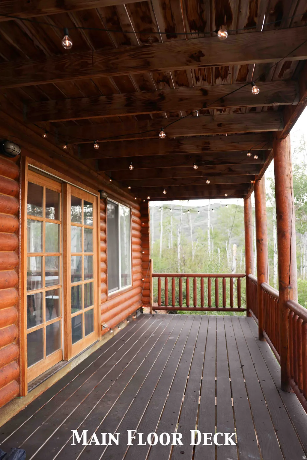Covered outdoor deck with dark wood-finish flooring, log siding exterior, and wood-framed French doors