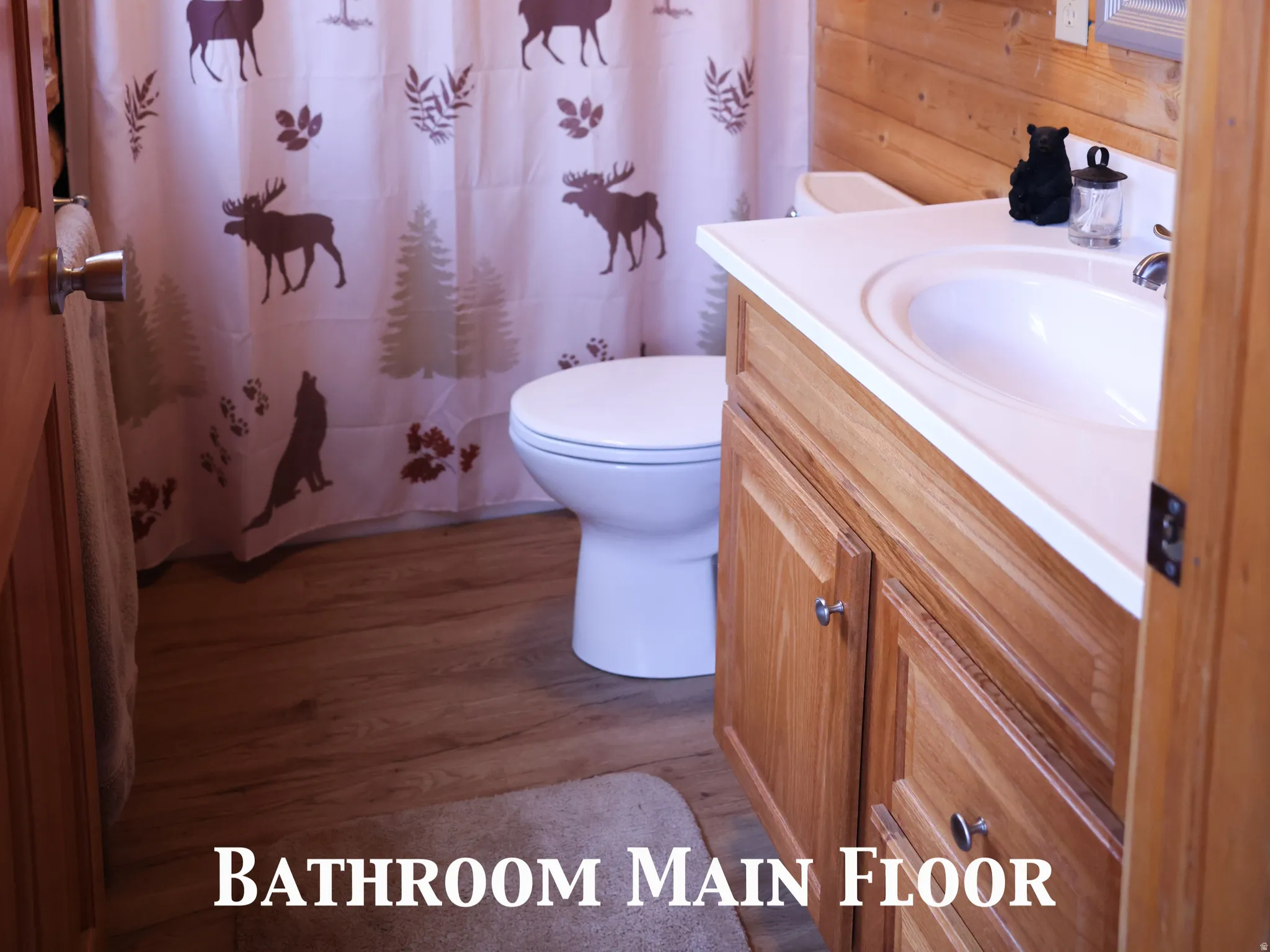 Bathroom featuring plank wood walls and ceiling, a single vanity with a white countertop and wood-finish cabinetry, a white toilet, and wood-finish flooring