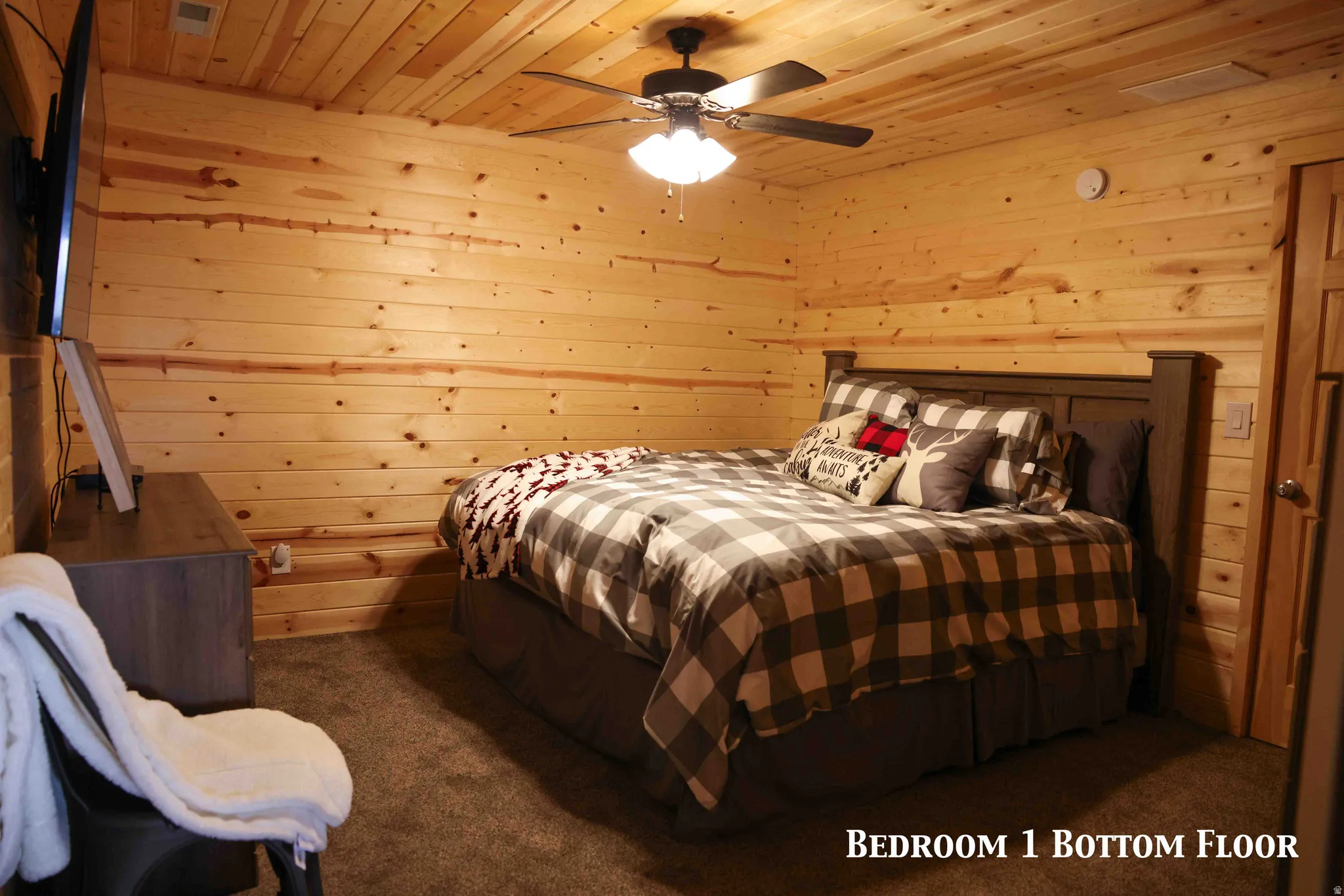 Bedroom featuring natural wood paneling on walls and ceiling, dark brown carpet flooring, and a ceiling fan with integrated lighting