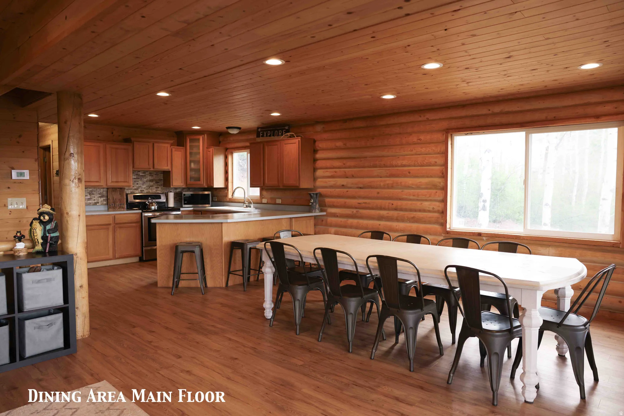 Open-concept dining area featuring wood-finish flooring, log walls, and a wood-paneled ceiling with recessed lighting