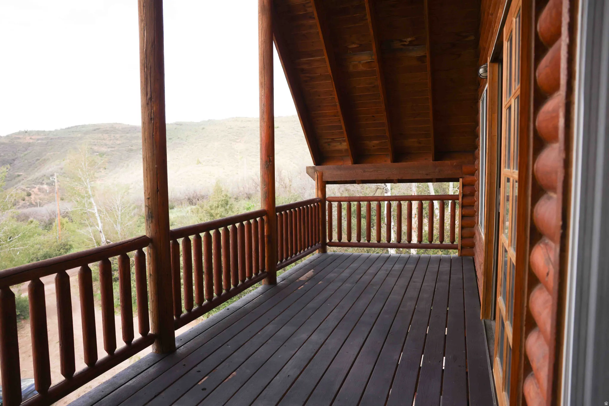 Expansive wooden deck featuring sturdy log railings and support beams, with a substantial wood-plank floor and a matching wood-paneled ceiling