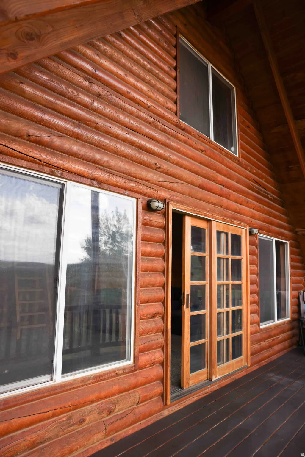 Exterior log siding with multiple windows and a wood-finish deck