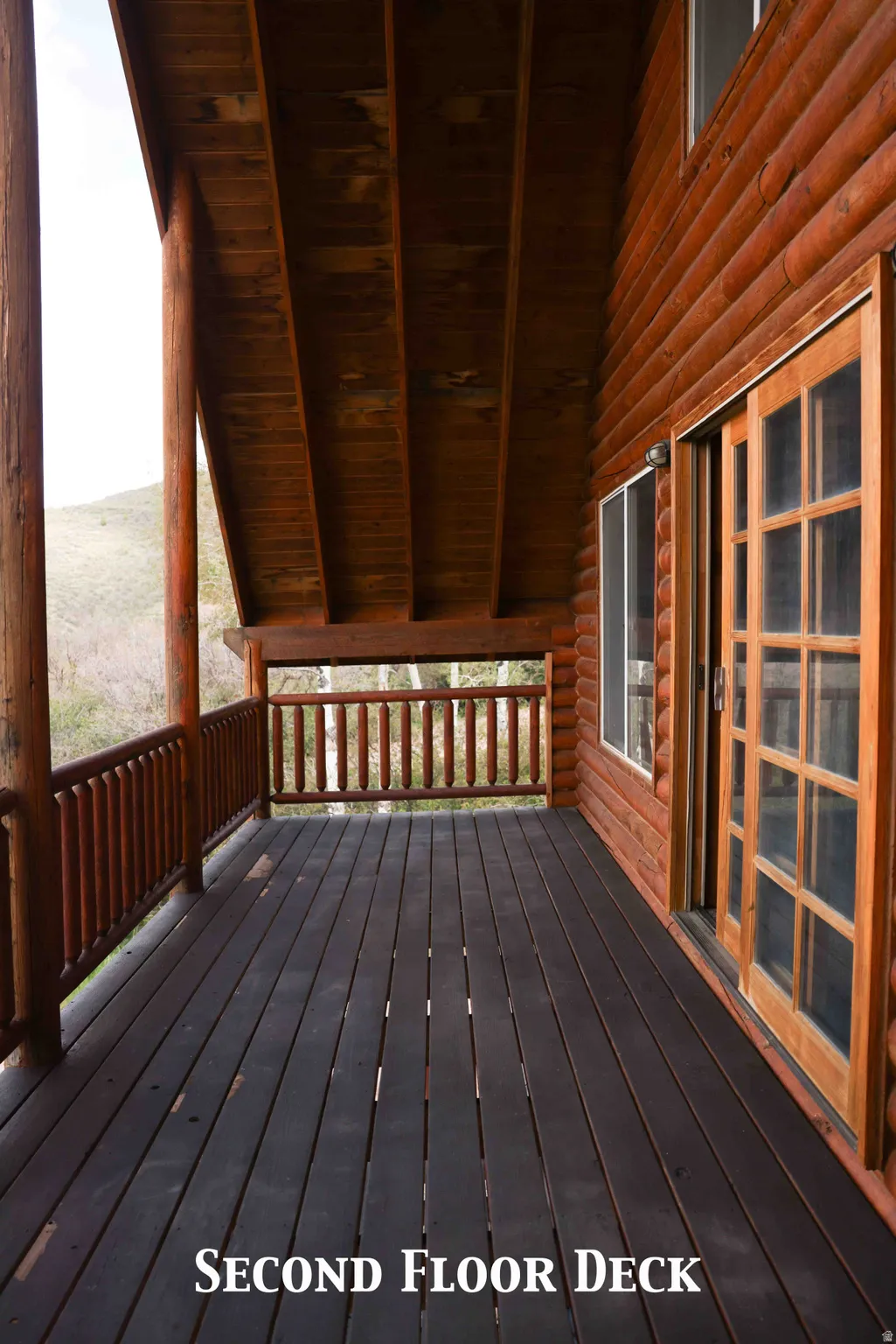 Spacious log-sided deck featuring dark-stained wood flooring, natural wood railings, and a wood-paneled ceiling
