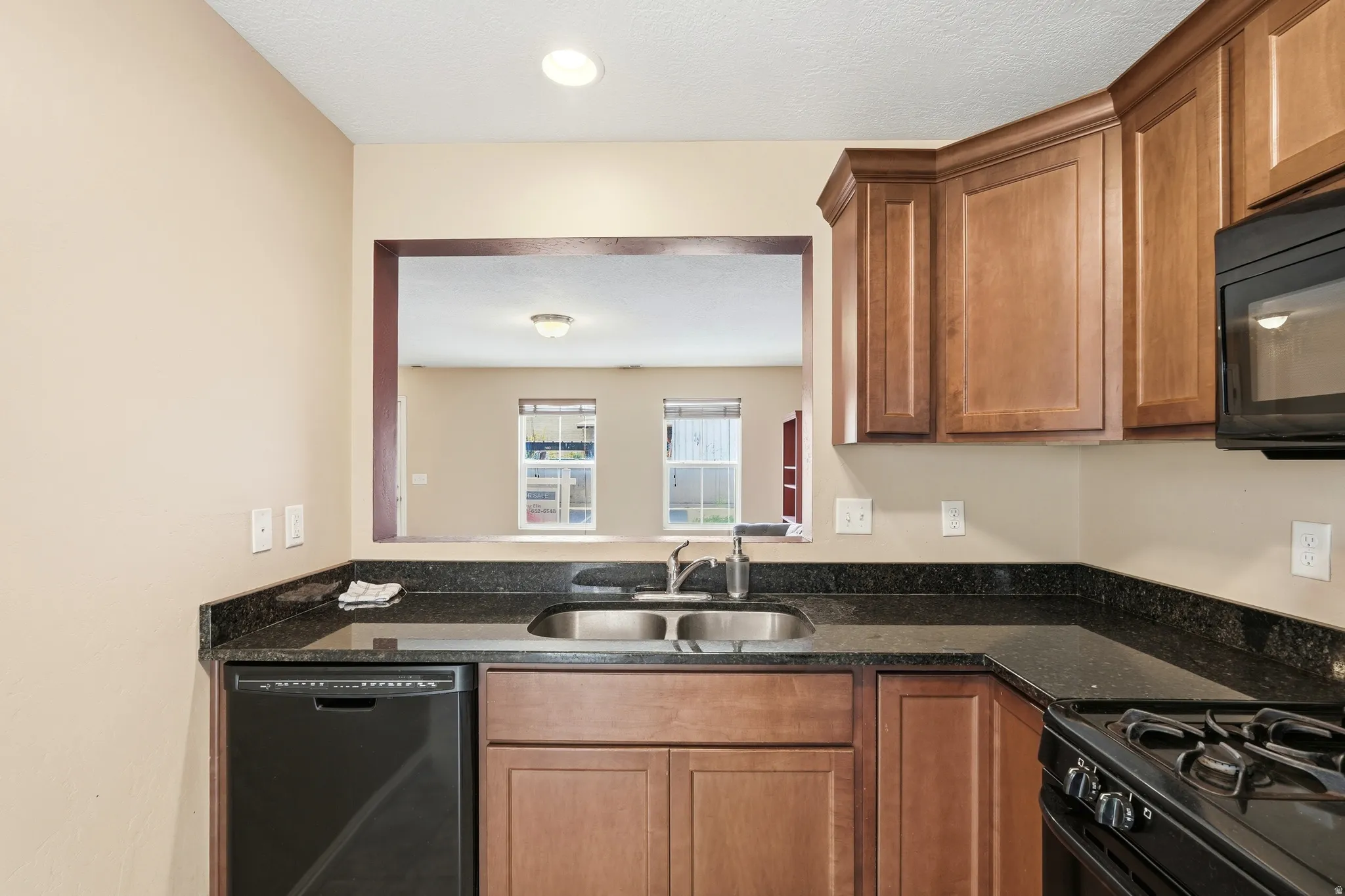 Kitchen featuring wood cabinetry, black appliances, a pass-through window, and a tile floor