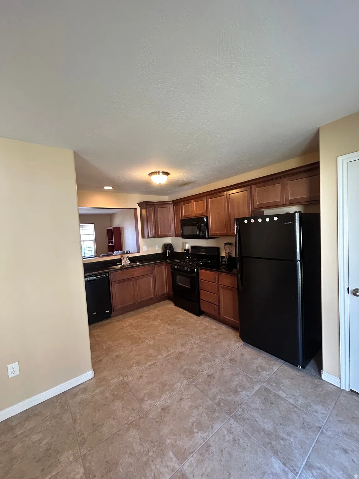 Kitchen featuring wood-finish cabinetry, black appliances, dark countertops, and tile flooring