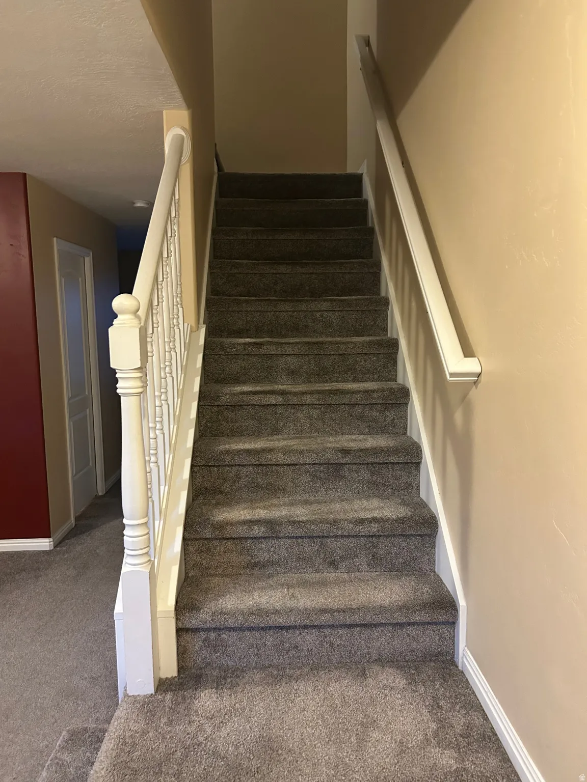Carpeted staircase featuring white balusters and a matching handrail