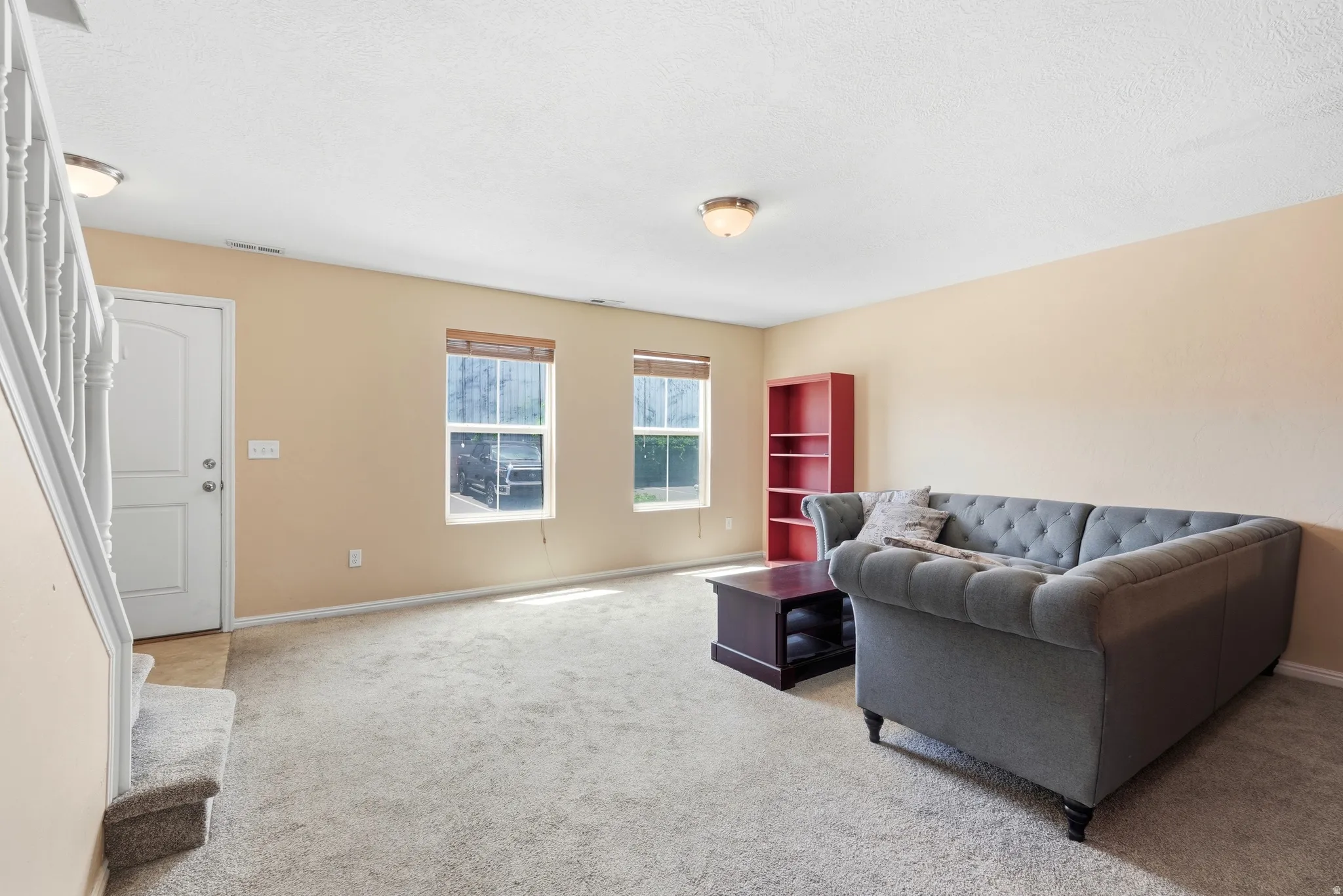 Carpeted living area featuring two windows, a white entry door, and a staircase with white banisters