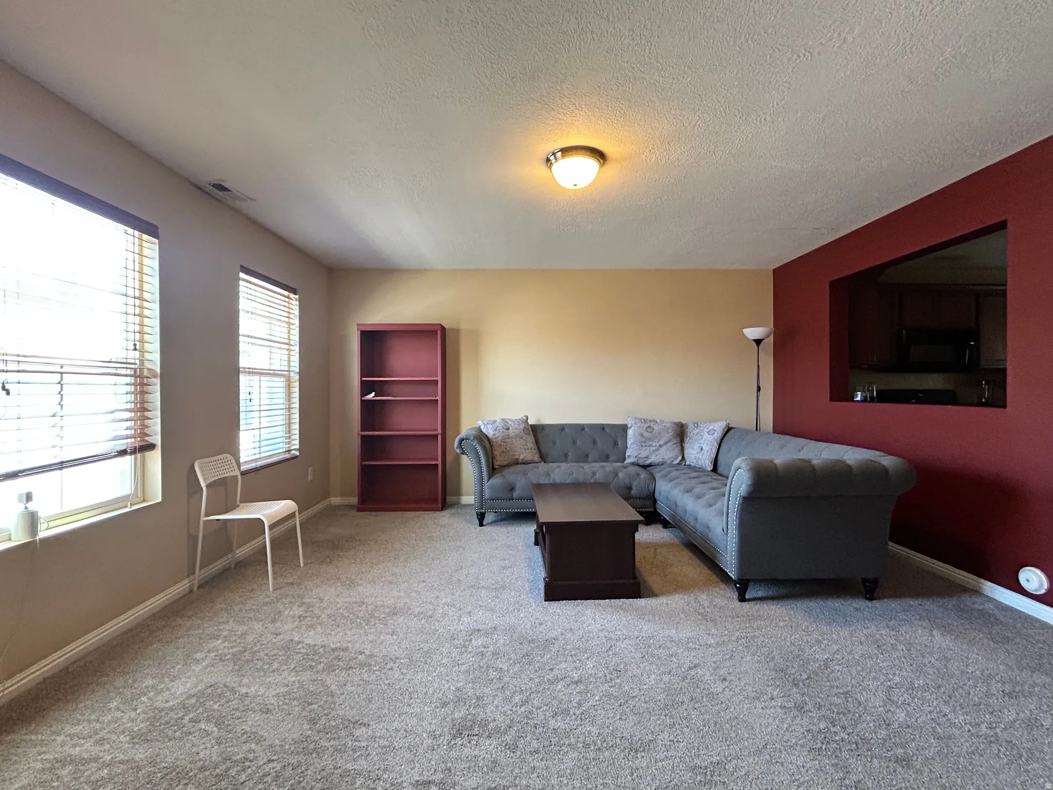 Bright living area featuring carpet, multiple windows with blinds, a contrasting accent wall, and a pass-through opening to the kitchen