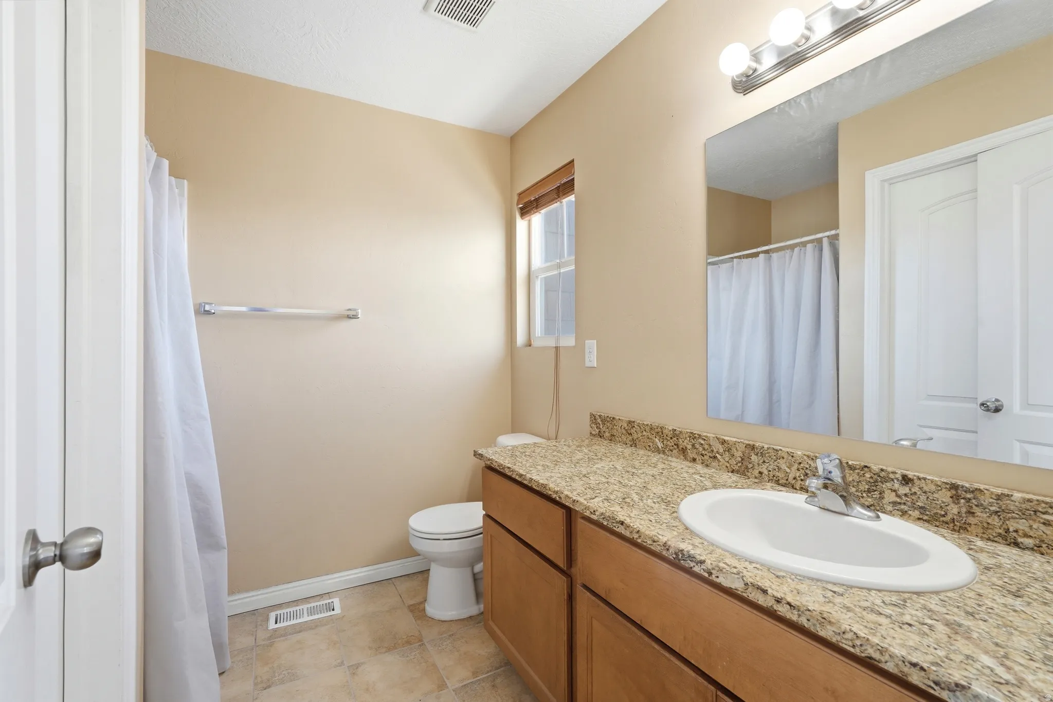 Master bathroom featuring a single vanity with an integrated sink, granite-finish countertop, and light wood cabinetry