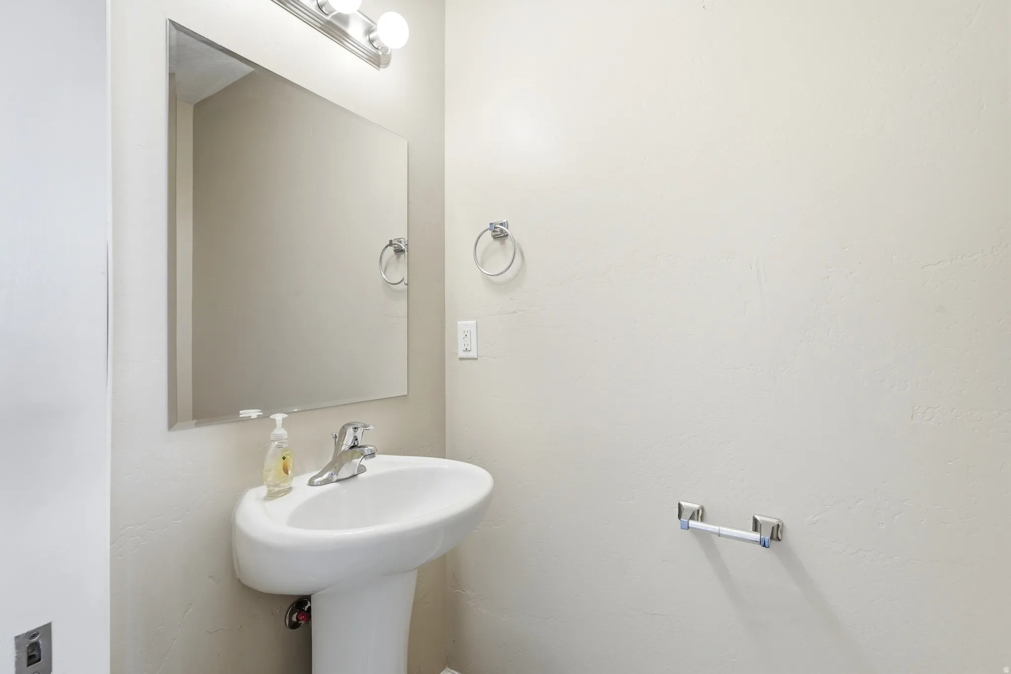 Pedestal sink with a polished chrome faucet, rectangular wall mirror, and modern vanity lighting