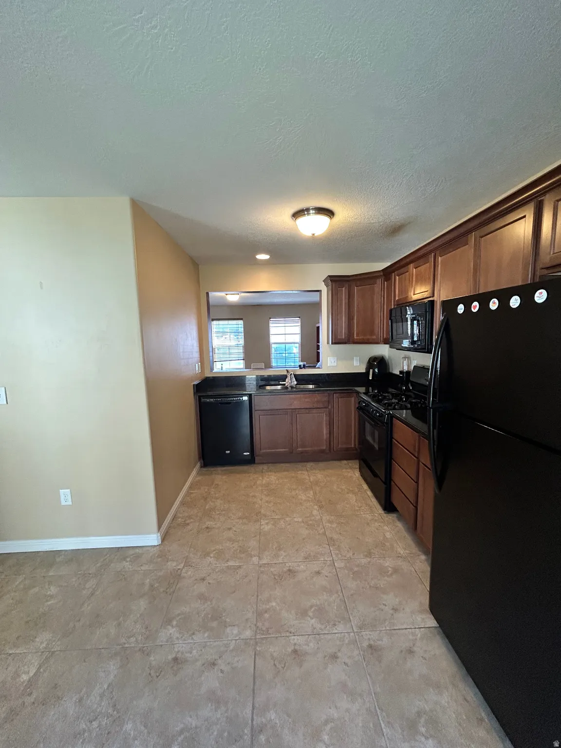 Kitchen featuring wood-finish cabinetry, black appliances, dark countertops, and tile flooring