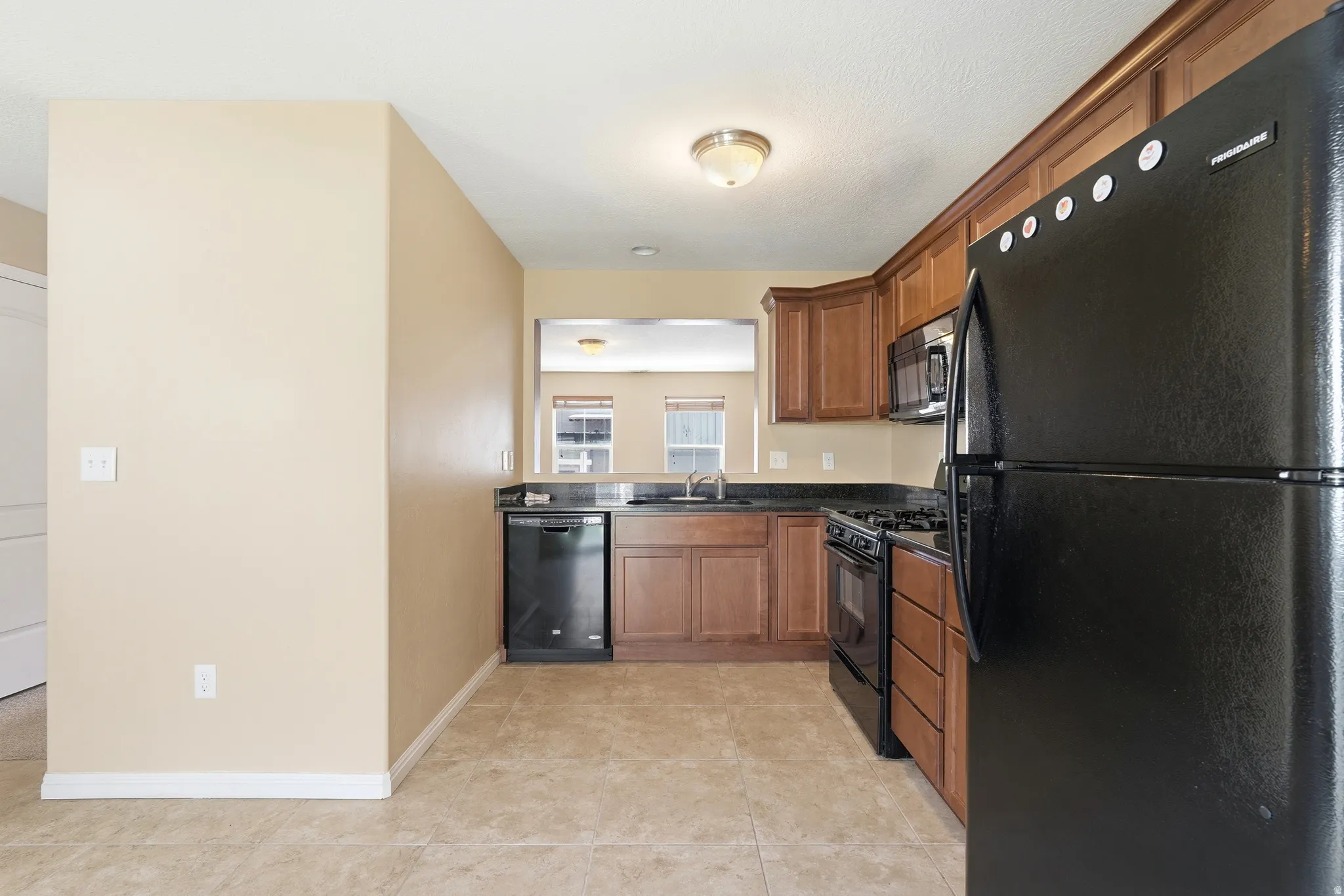 Kitchen featuring wood cabinetry, black appliances, a pass-through window, and a tile floor