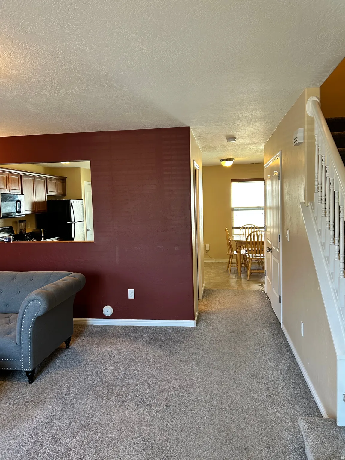 Carpeted living area with a half wall featuring a pass-through opening to the kitchen