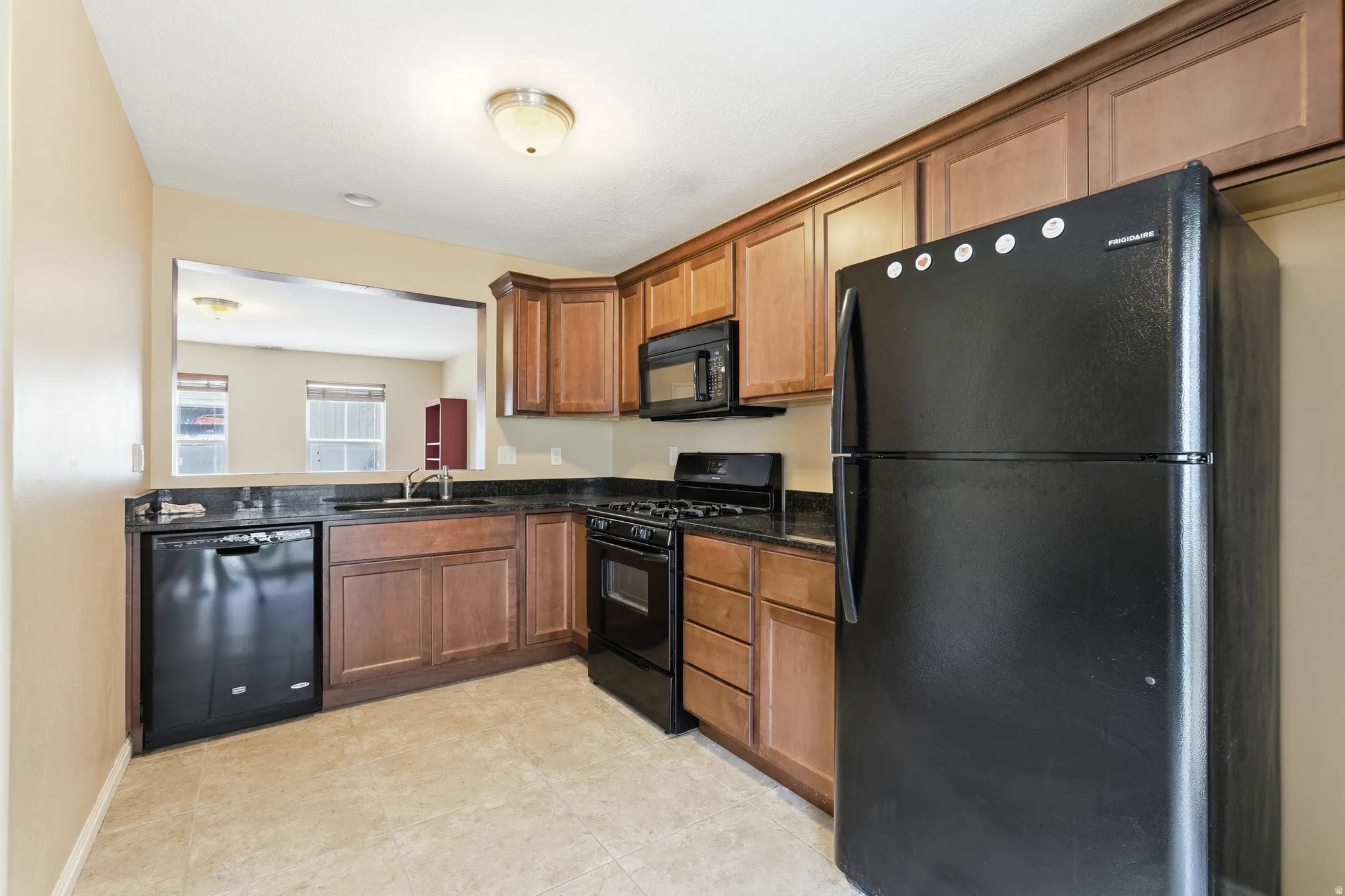 Kitchen featuring wood cabinetry, black appliances, a pass-through window, and a tile floor
