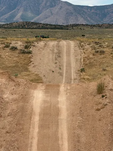 Unpaved dirt road on a barren landscape with distant mountains