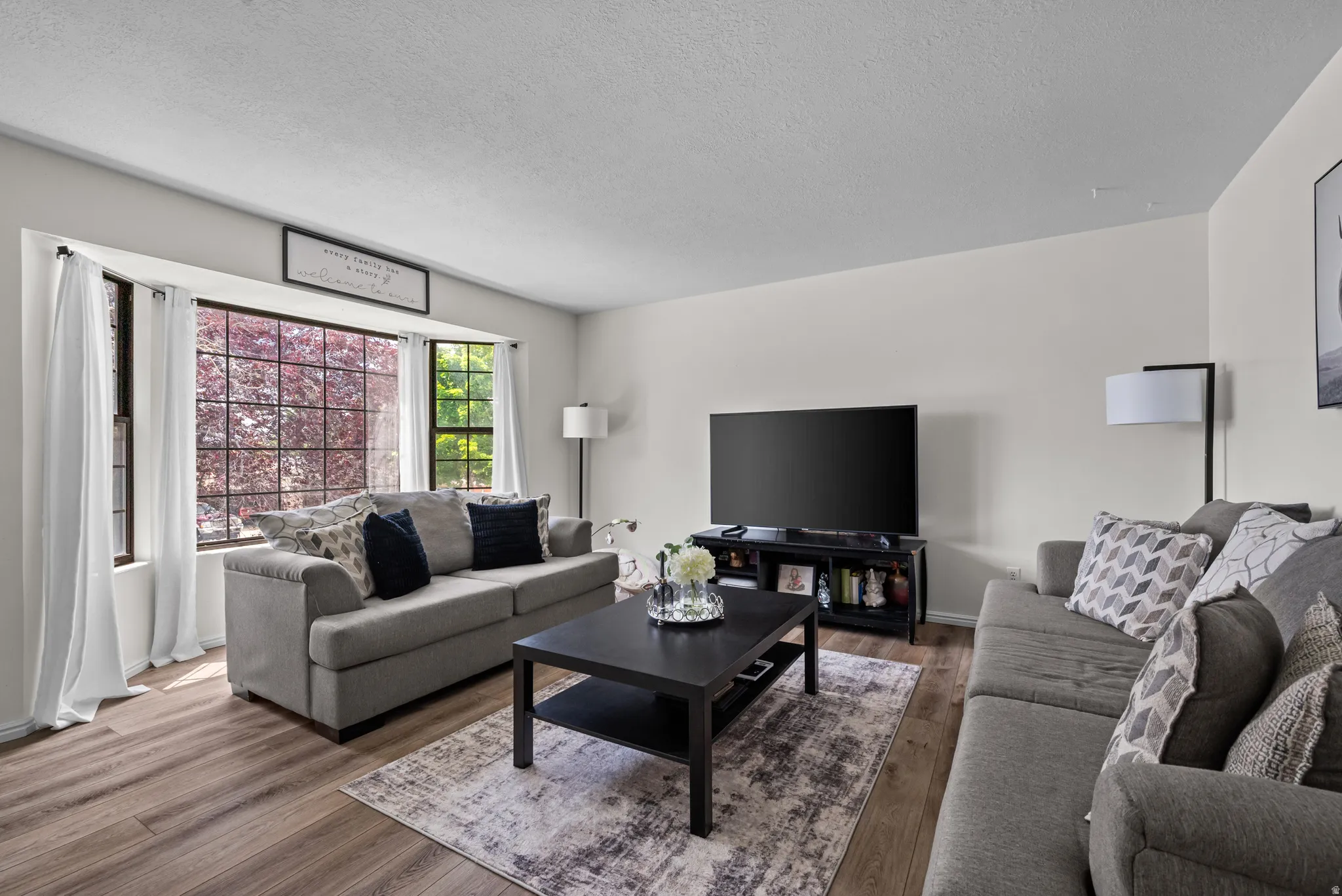 Spacious living area featuring wood-finish flooring, light-toned walls, and a large bay window