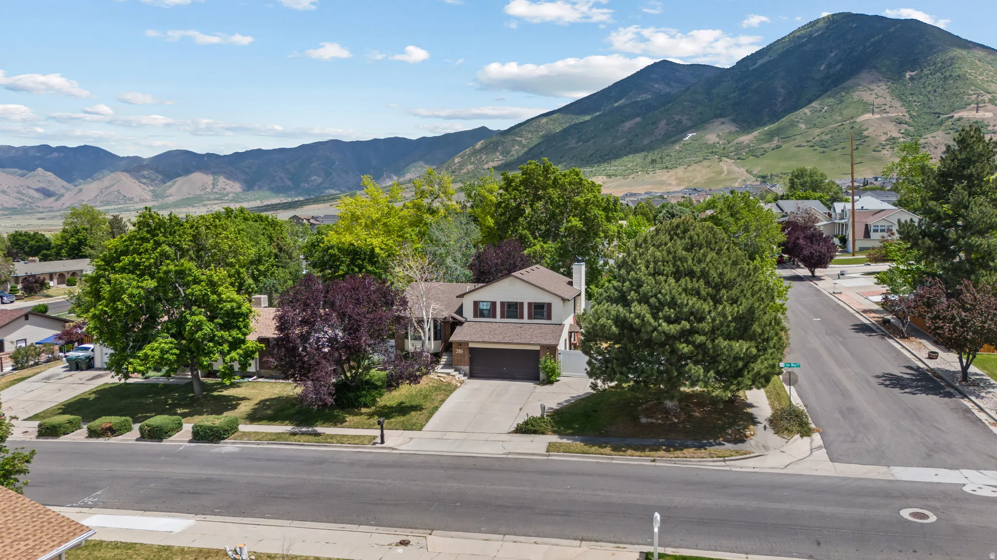 Two-story residence featuring a two-car garage, mature landscaping, paved driveway, and mountain backdrop