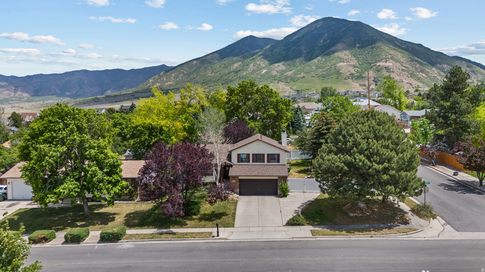 Mountain backdrop property featuring a two-story residence with a two-car garage, mature landscaping, and an asphalt driveway