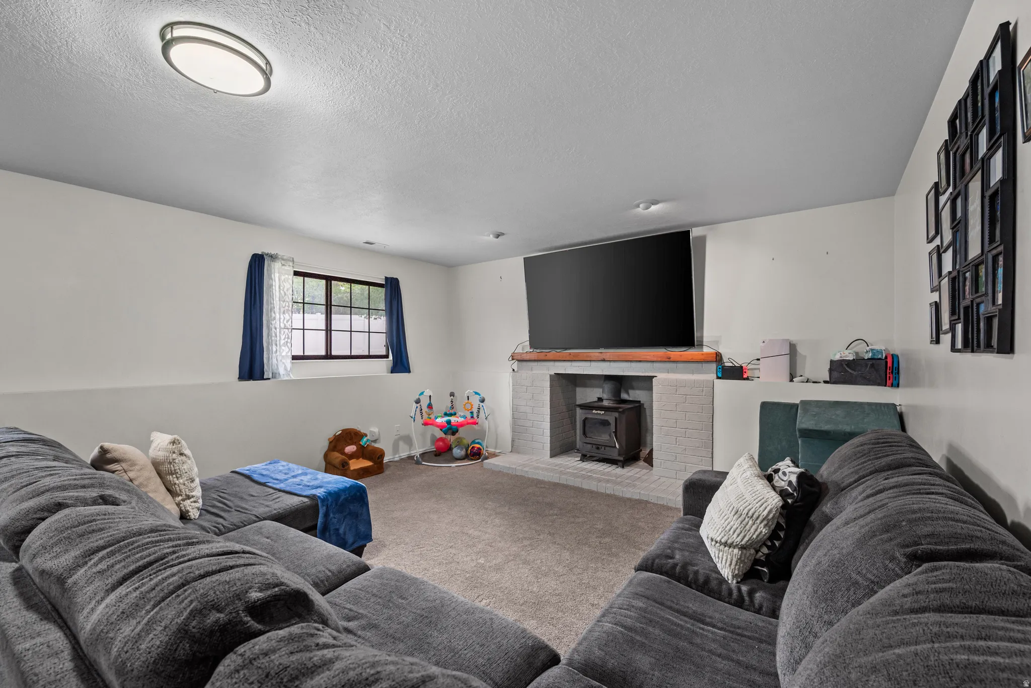 Spacious living area featuring neutral carpeting, white walls, a window with dark trim, a built-in fireplace with a wood mantel, and an oval ceiling light fixture