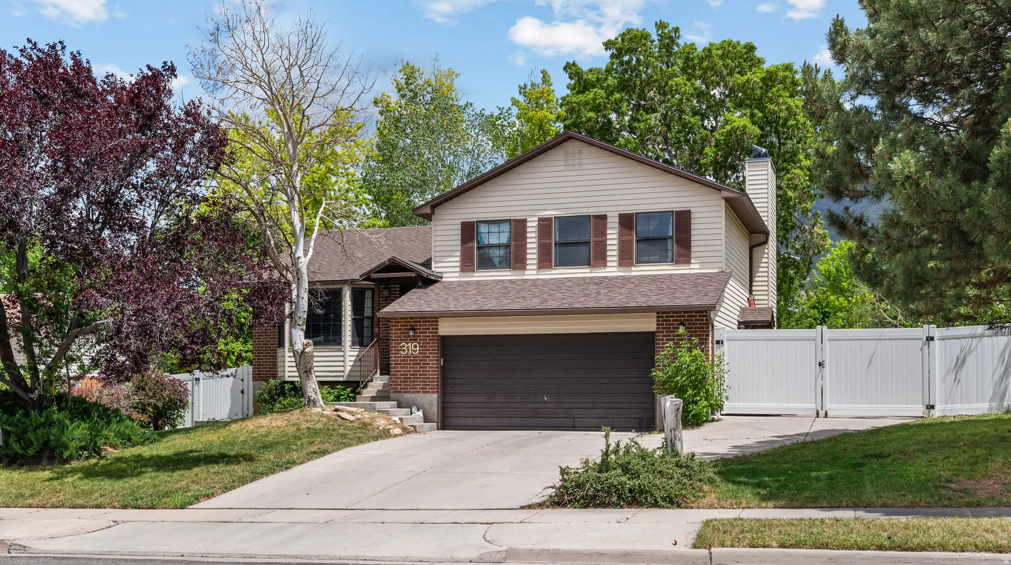 Split-level residence featuring a two-car garage with a brown door, tan siding, and a brick facade