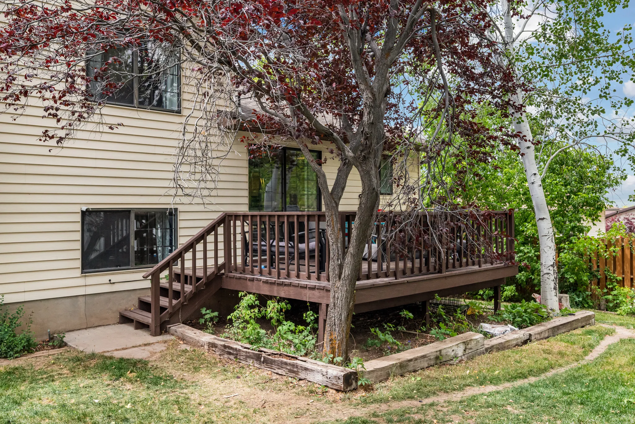 Rear exterior featuring a spacious wood-finish deck with railing, stairs, and mature trees