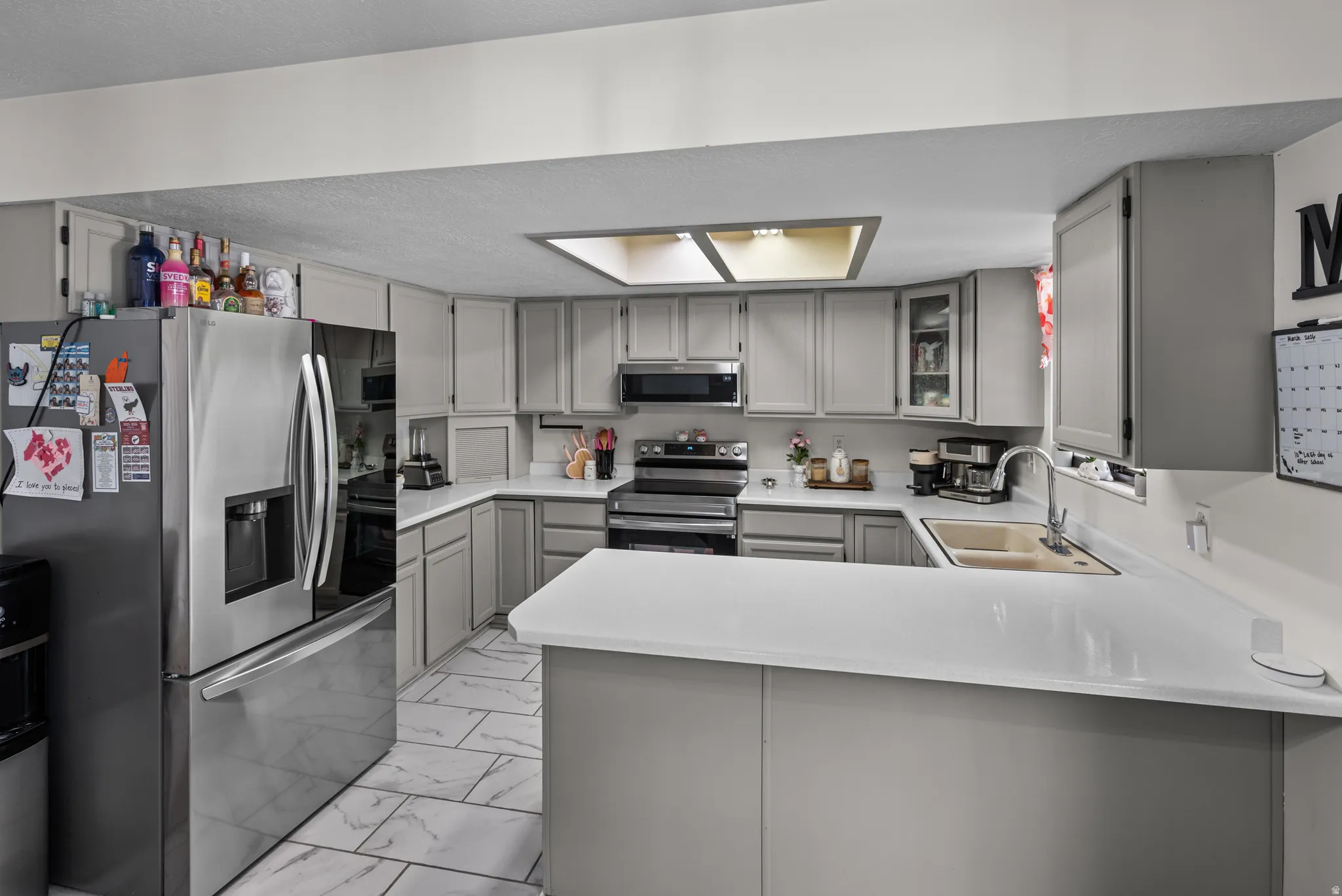 Kitchen featuring an L-shaped counter with white countertops, grey cabinetry, stainless steel appliances, and a rectangular skylight