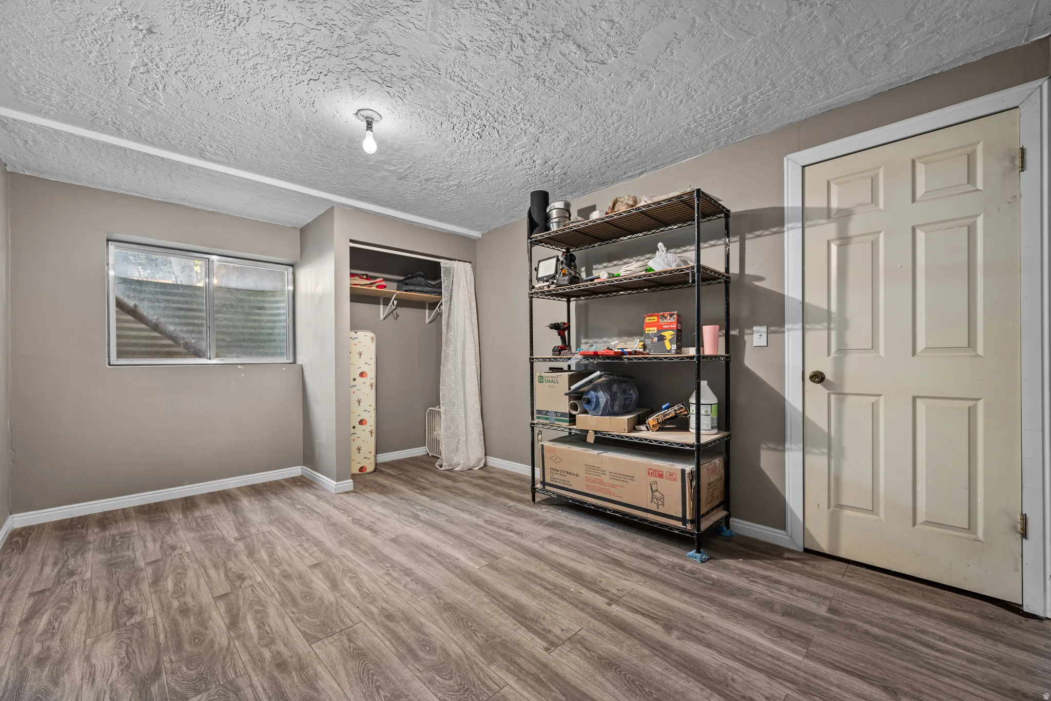 Room featuring wood-finish flooring, a window with a security grate, a closet with a hanging rod, and a six-panel interior door
