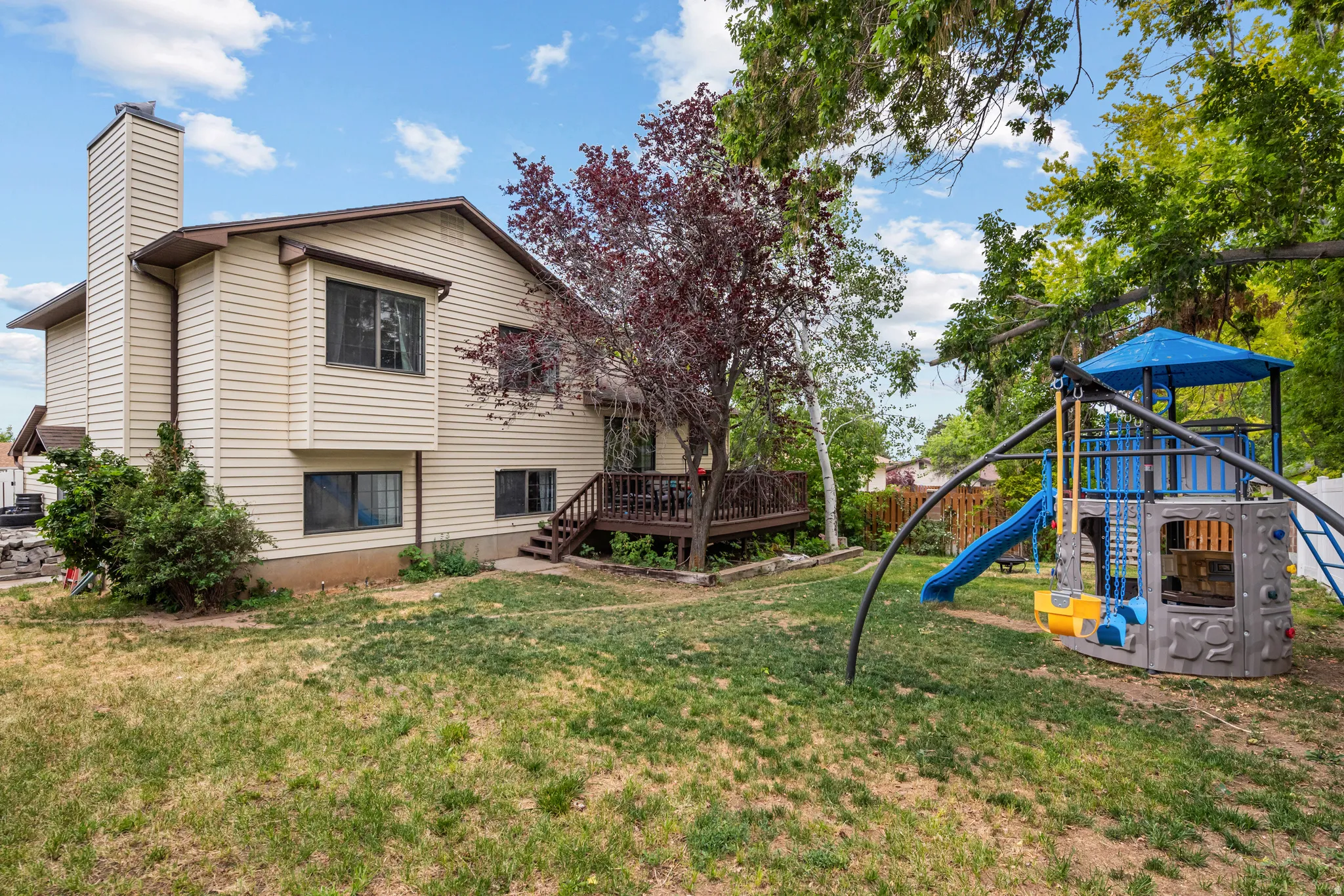 Expansive backyard featuring a wood deck, mature trees, and a play structure