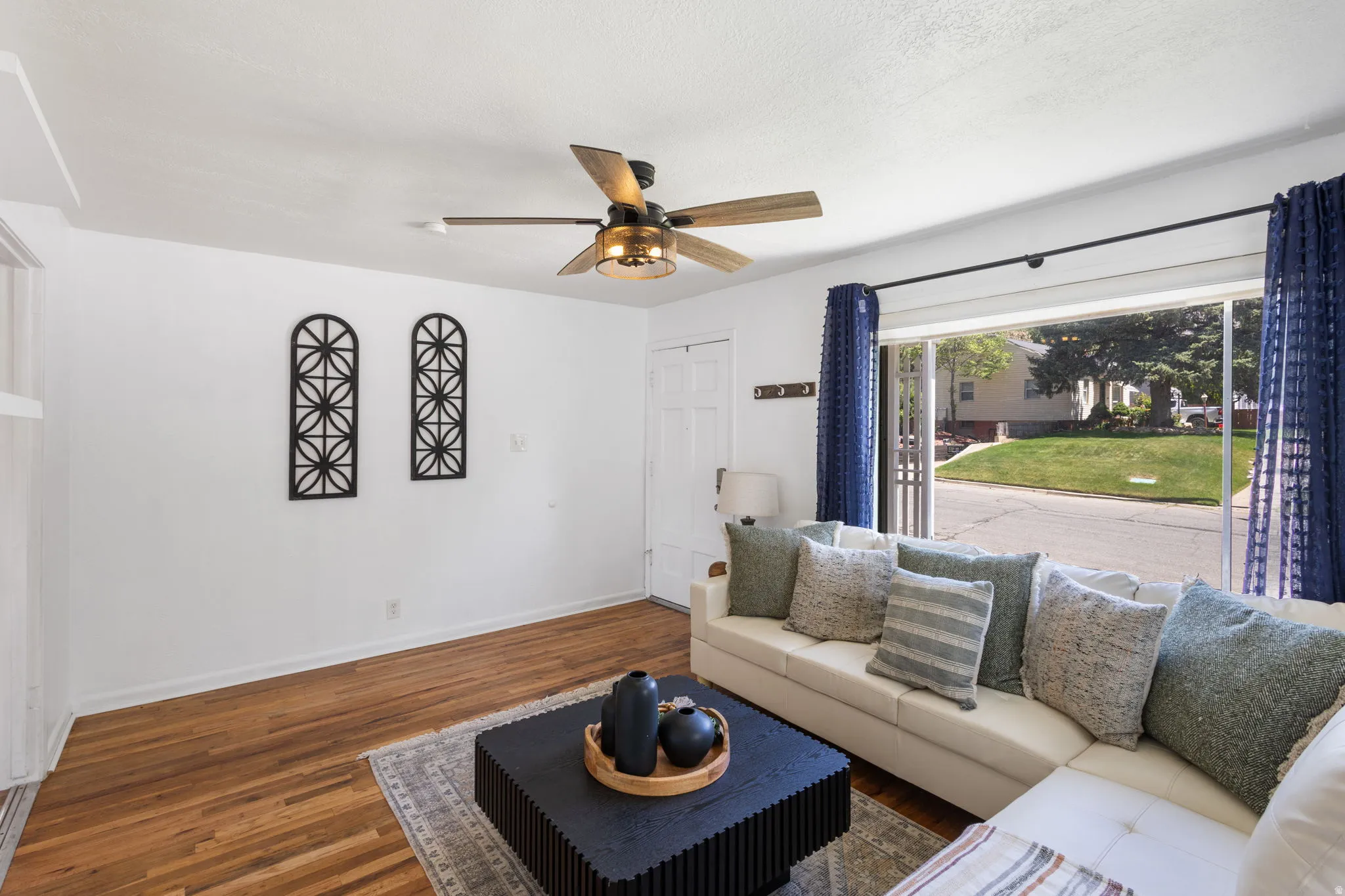 Living area featuring hardwood flooring, a ceiling fan with integrated lighting, and a large window offering exterior views
