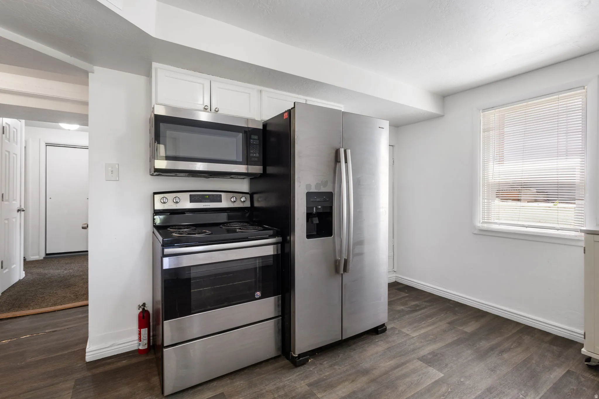 Kitchen area featuring LVP flooring, white cabinetry, and stainless steel appliances including a side-by-side refrigerator, electric range, and built-in microwave