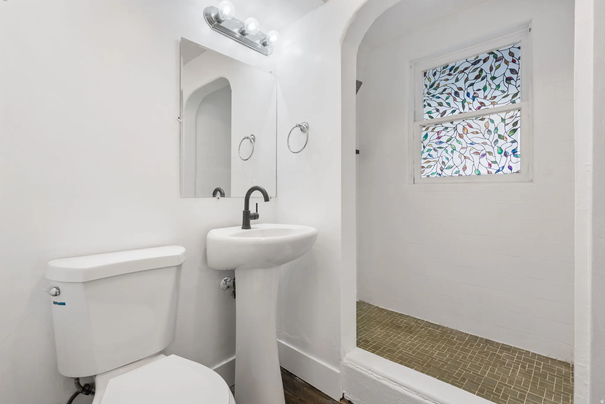 Bathroom featuring a pedestal sink with a matte black faucet, a wall-mounted mirror, and overhead vanity lighting