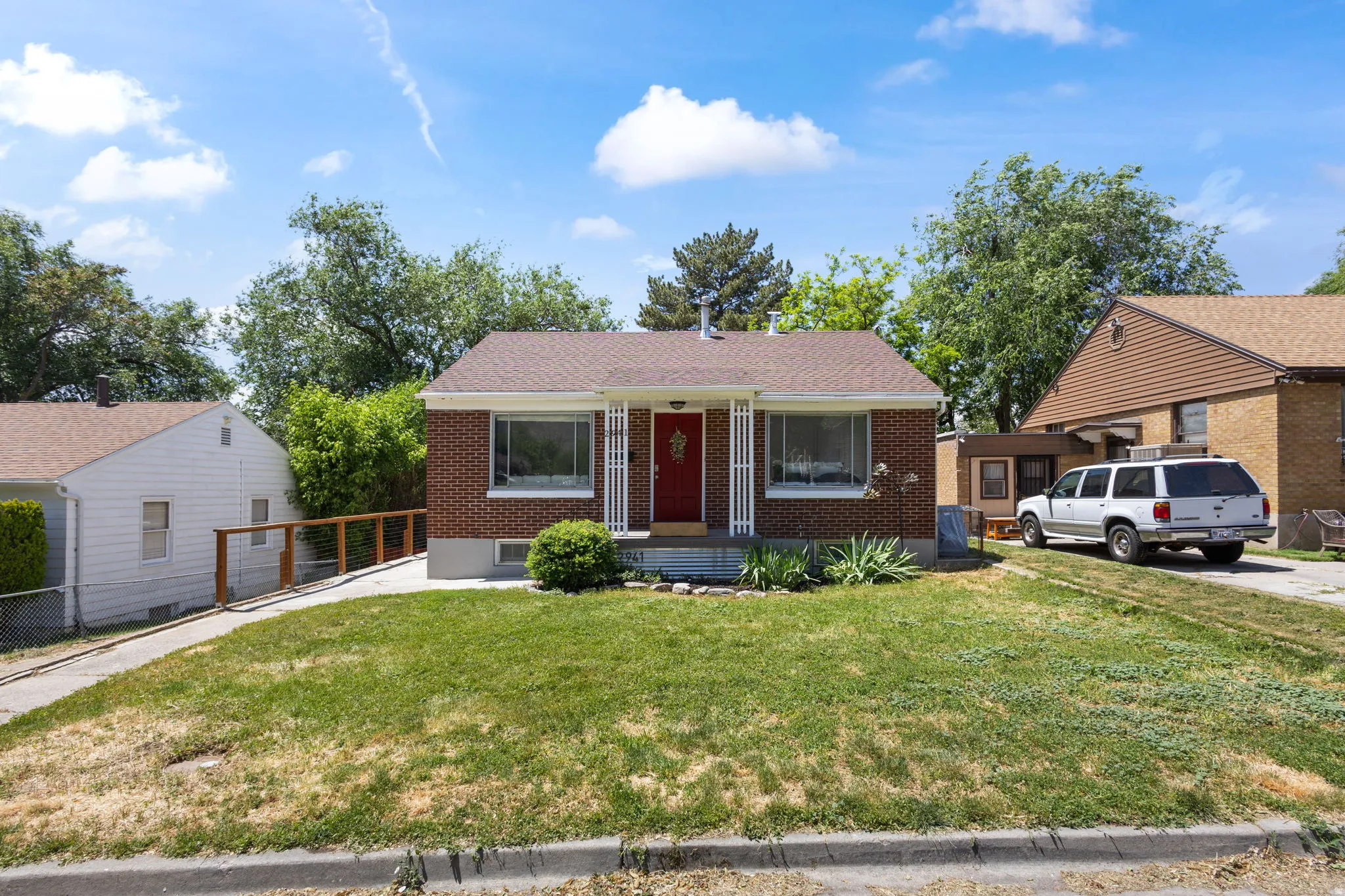 Brick exterior home featuring a red front door, covered porch with white columns, and a front yard with mature landscaping.