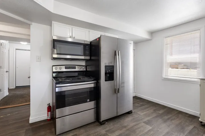 Kitchen area featuring LVP flooring, white cabinetry, and stainless steel appliances including a side-by-side refrigerator, electric range, and built-in microwave