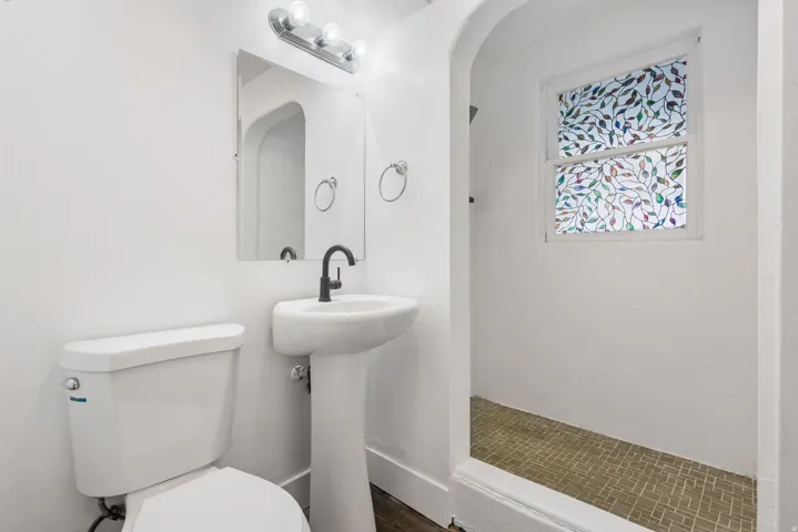 Bathroom featuring a pedestal sink with a matte black faucet, a wall-mounted mirror, and overhead vanity lighting
