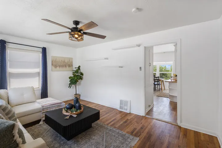 Living space featuring hardwood flooring, white walls, and a contemporary ceiling fan with integrated lighting