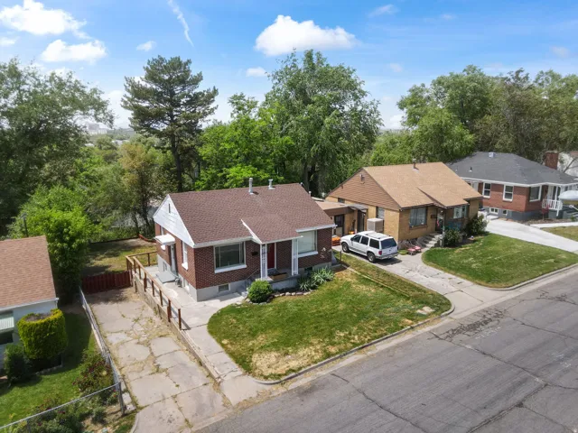 Brick exterior residence featuring a brown shingle roof, established front lawn, concrete driveway, and mature landscaping