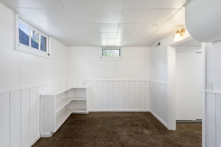 Finished room featuring white wainscoting, built-in shelving, white ceiling tiles, and two windows