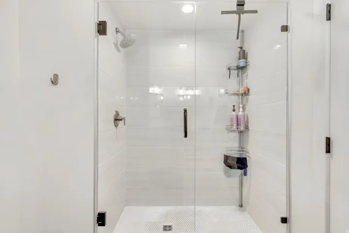 Glass-enclosed shower featuring large format white wall tiling and a hexagonal mosaic floor