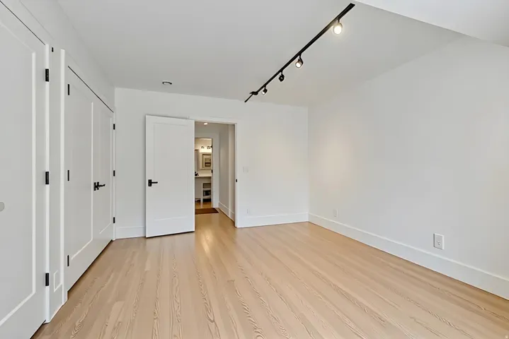Room featuring light wood-finish flooring, white walls, and a black track lighting fixture