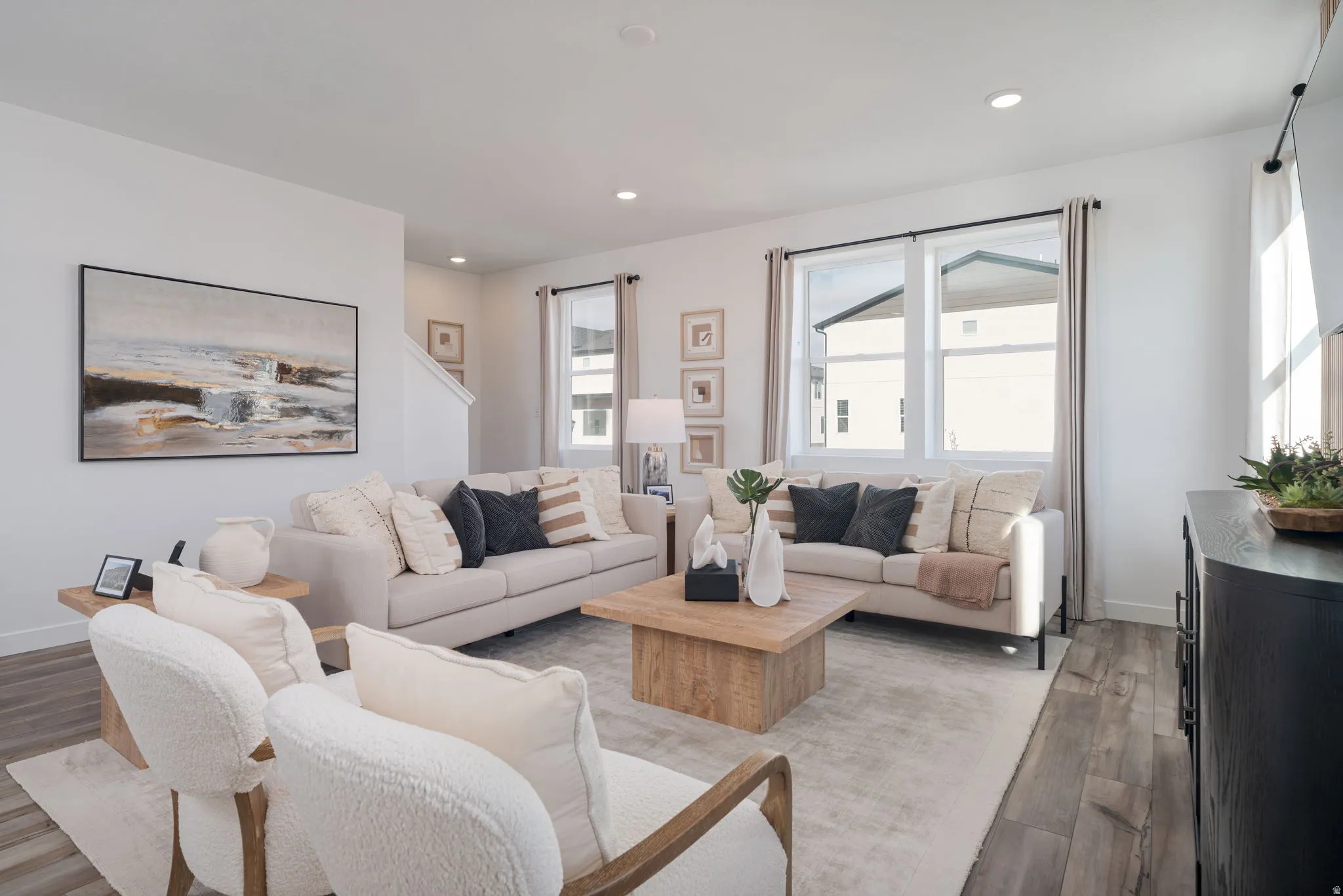 Open-concept living area featuring light wood-finish flooring, recessed lighting, and large windows with privacy drapes