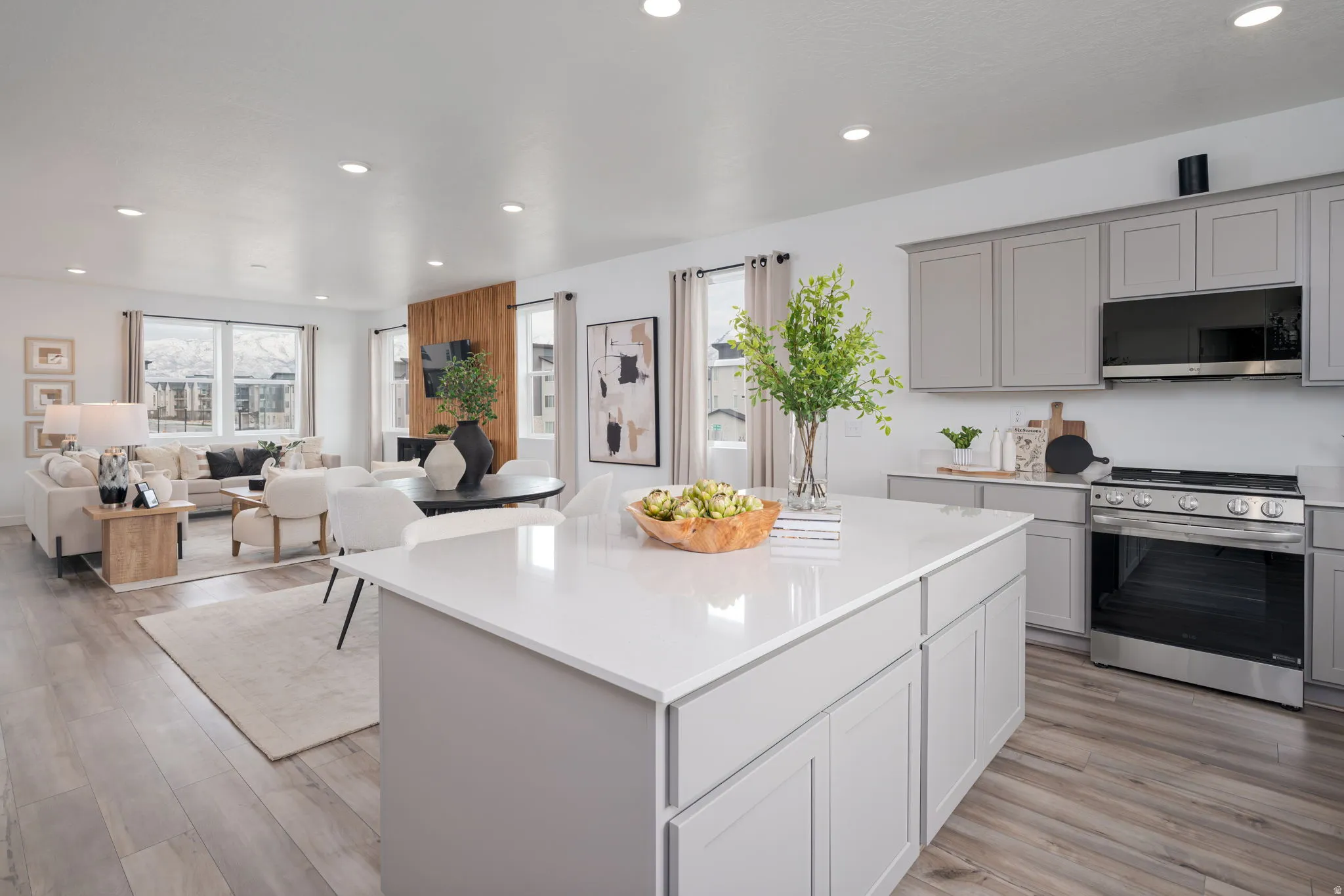 Open-concept living space featuring a kitchen island with a white countertop, light gray cabinetry, stainless steel appliances, and wood-finish flooring throughout