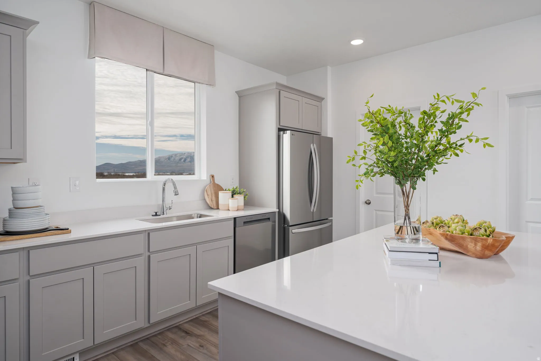 Modern kitchen featuring light gray cabinetry, stainless steel appliances, white countertops, and wood-finish flooring