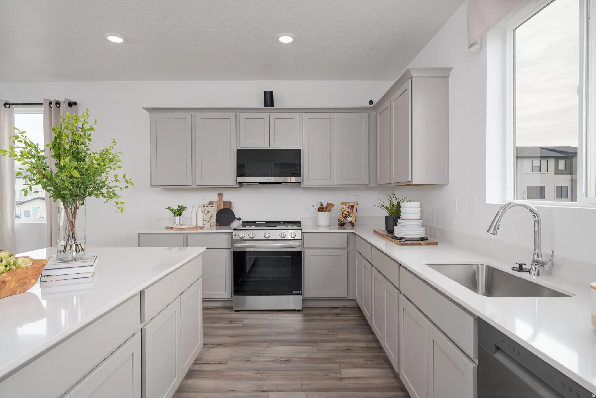 Kitchen featuring light-toned cabinetry, a spacious center island with a white countertop, stainless steel appliances, a stainless steel sink with a high-arc faucet, and wood-finish flooring