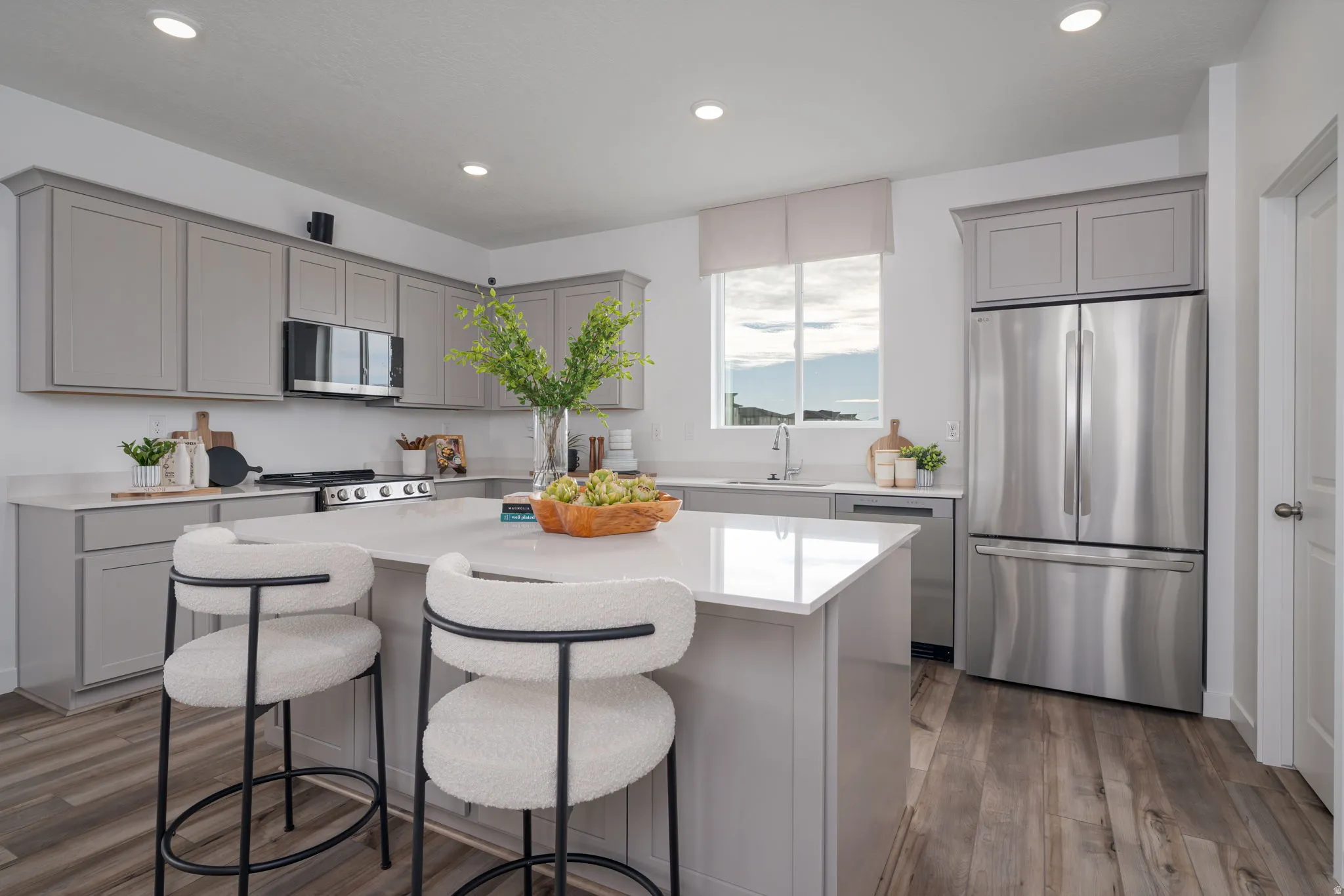 Kitchen featuring a central island with countertop seating, stainless steel appliances, light gray cabinetry, light countertops, and wood-finish flooring