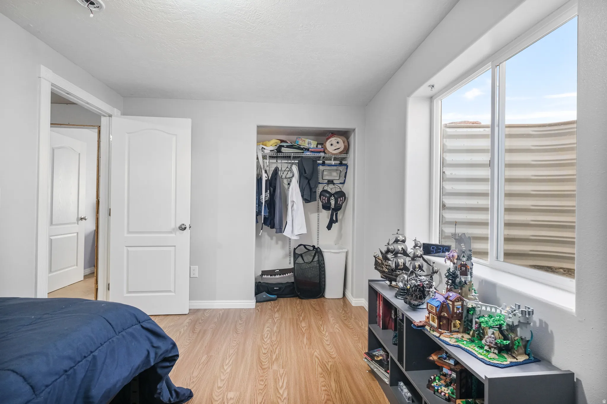 Bright bedroom featuring wood-finish flooring, a white window frame, and light gray walls